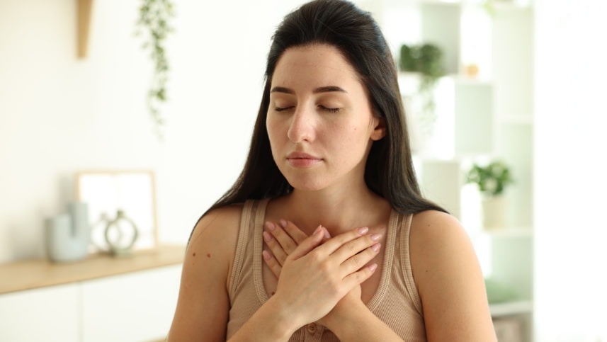 Mulher com duas mãos cruzadas no busto e rosto relaxado após alívio de um episódio de síndrome do pânico