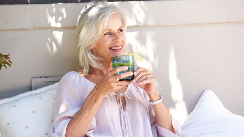 Mulher da terceira idade sorrindo com xícara na mão após alívio de sintomas de alterações hormonais