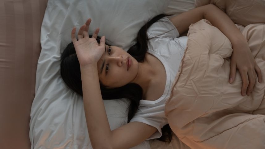 Mulher deitada com mão na cabeça preocupada por estar com insônia