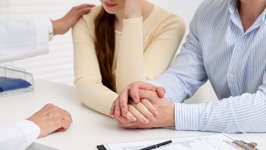 Mulher em consulta com o médico especialista em infertilidade, de mãos dadas com um homem